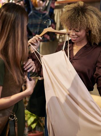 Vrouw laat jurk zien door deze voor zich te houden in een kledingwinkel