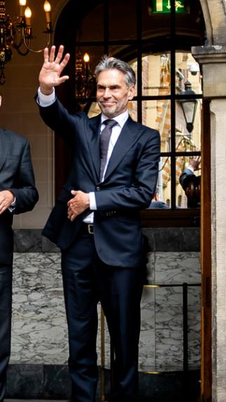 Een foto van premier Rutte die wegfietst bij het Torentje, en Schoof en iemand anders die hem uitzwaaien vanaf de boog bij de uitgang.