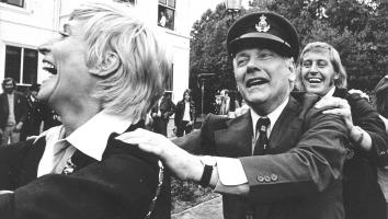 Zwartwit-foto van oud-premier Den Uyl die lachend meedoet aan een polonaise met voetballers in de tuin van het Catshuis.