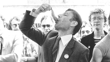 Zwartwit-foto van oud-premier Van Agt die op straat een haring eet.