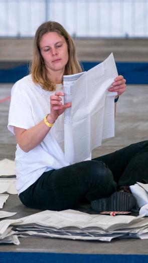 Een burger is stemmen aan het tellen. Ze zit op de grond met een stembiljet in haar handen en stembiljetten om haar heen.