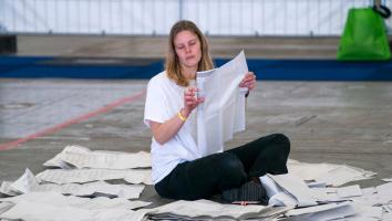 Een burger is stemmen aan het tellen. Ze zit op de grond met een stembiljet in haar handen en stembiljetten om haar heen.