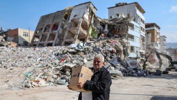 Een man loopt met een verhuisdoos langs een ingestort gebouw en puin