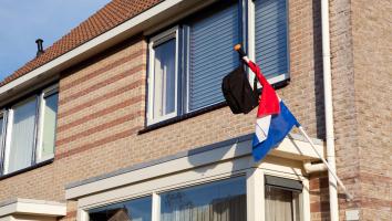 Een schooltas hangt aan een Nederlandse vlag, die aan een huis is bevestigd.