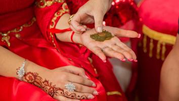 Een vrouw in rode kleding krijgt henna met een muntje in haar hand