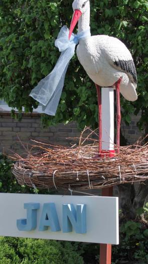Een ooievaarsbeeld in een nest in iemands voortuin, met daaronder de kindernaam 'Jan'. 