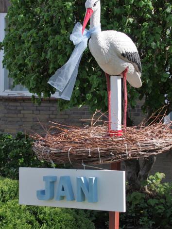 Een ooievaarsbeeld in een nest in iemands voortuin, met daaronder de kindernaam 'Jan'. 