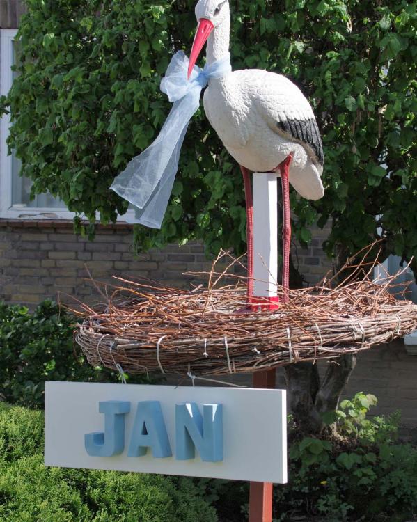Een ooievaarsbeeld in een nest in iemands voortuin, met daaronder de kindernaam 'Jan'.