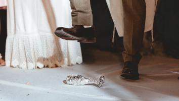 Een glas in folie gewikkeld met daarboven een schoen van iemand die op het punt staat het glas kapot te trappen.