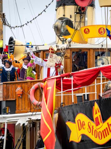 Sinterklaas en roetveegpieten zwaaien vanaf de versierde stoomboot naar publiek.