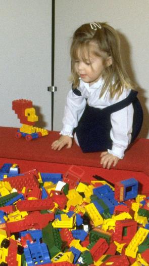 Twee meisjes spelen met lego in de jaren 80, voor hen een grote bak met felgekleurde legostenen.
