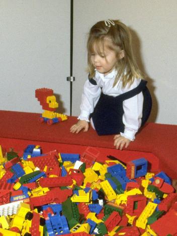 Twee meisjes spelen met lego in de jaren 80, voor hen een grote bak met felgekleurde legostenen.