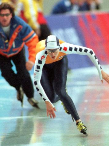 Schaatser Marianne Timmer schaatst vol concentratie op de baan, achter haar is een coach te zien.