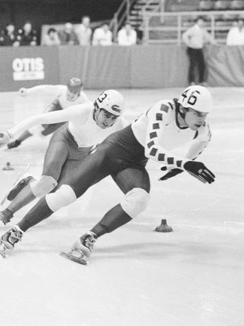 Een zwart-witfoto van shorttrackers aan het racen op de ijsbaan