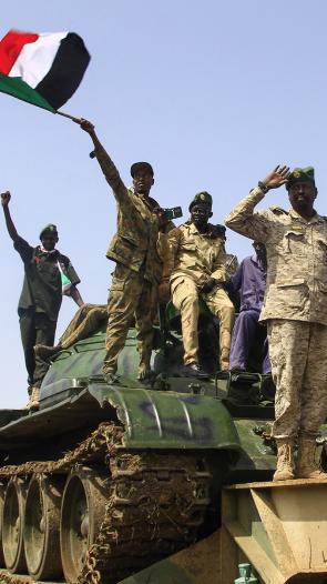 Vier mannen in legeruniform van het Sudanese regeringsleger staan op een tank en een zwaait met Sudanese vlag