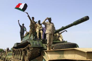 Vier mannen in legeruniform van het Sudanese regeringsleger staan op een tank en een zwaait met Sudanese vlag