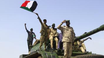Vier mannen in legeruniform van het Sudanese regeringsleger staan op een tank en een zwaait met Sudanese vlag