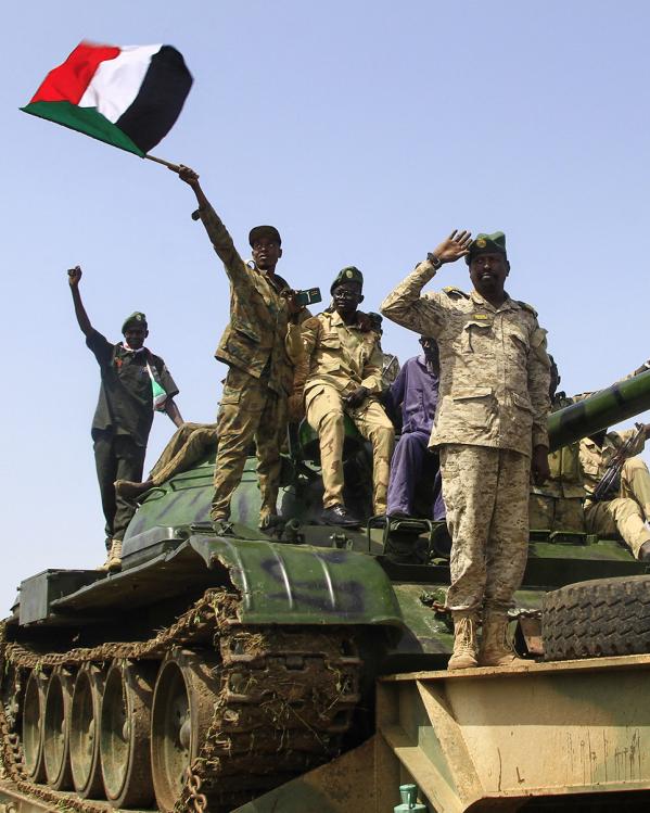 Vier mannen in legeruniform van het Sudanese regeringsleger staan op een tank en een zwaait met Sudanese vlag