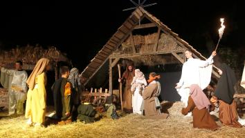 Een levende kerststal in de avond, met onder andere Maria, Jozef, Jezus en andere Bijbelse figuren eromheen