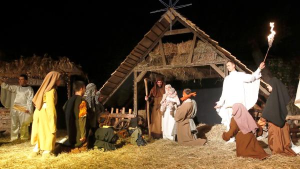 Een levende kerststal in de avond, met onder andere Maria, Jozef, Jezus en andere Bijbelse figuren eromheen