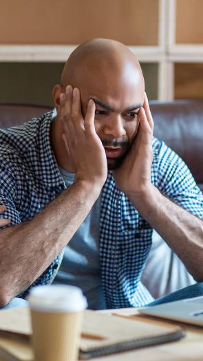Man kijkt gefrustreerd naar laptop met handen tegen zijn kale hoofd aan. Vrouw naast hem legt hand op schouder om hem gerust te stellen