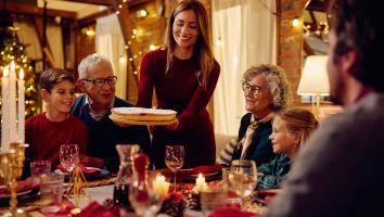 Familie aan het dineren aan een tafel vol kaarsen. Met ouderen en kinderen. Jonge vrouw zet lachend een taart op tafel. 