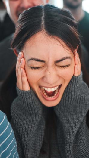 een meisje staat in het midden van een menigte te schreeuwen met haar handen op haar gezicht.