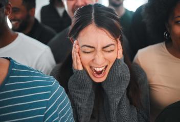 een meisje staat in het midden van een menigte te schreeuwen met haar handen op haar gezicht.