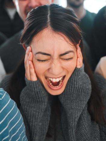 een meisje staat in het midden van een menigte te schreeuwen met haar handen op haar gezicht.