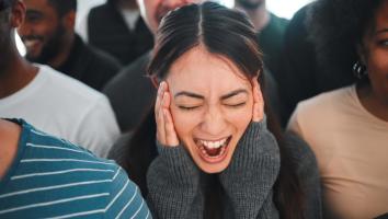 een meisje staat in het midden van een menigte te schreeuwen met haar handen op haar gezicht.