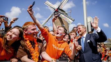 Koning Willem-Alexander maakt een selfie met mensen gekleed in oranje die bij een molen staan achter een hek
