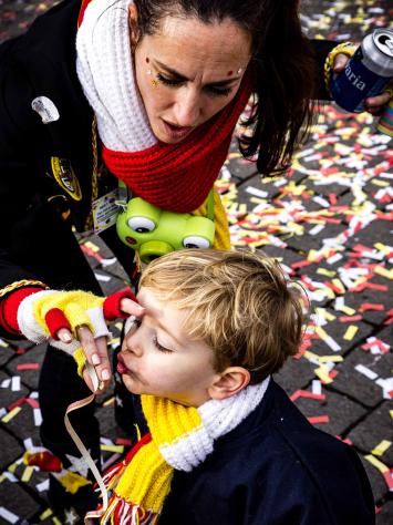 Een jongentje die met zijn moeder in Den Bosch carnaval viert en die een confetti rolletje uitblaast.