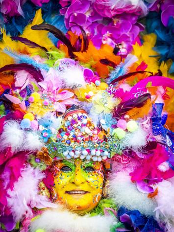 Een dame die verkleed is voor carnaval met schmink op haar gezicht en een grote hoed. 