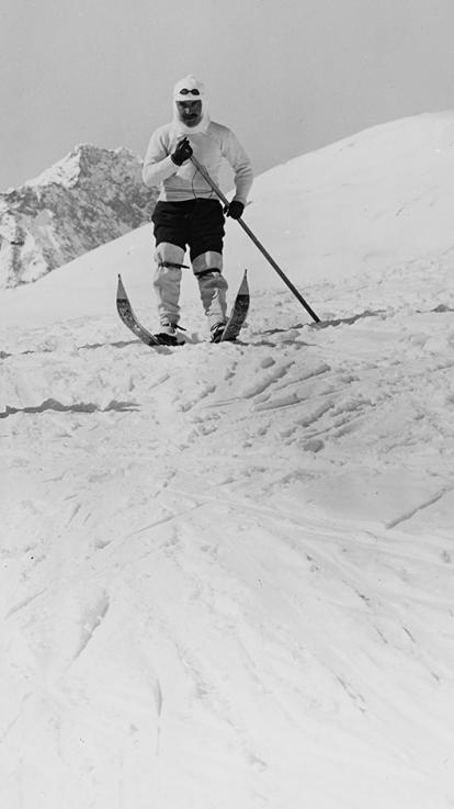 een zwart-witfoto van twee skiërs die eind 19e eeuw poseren voor de camera in de besneeuwde bergtoppen van de Alpen.