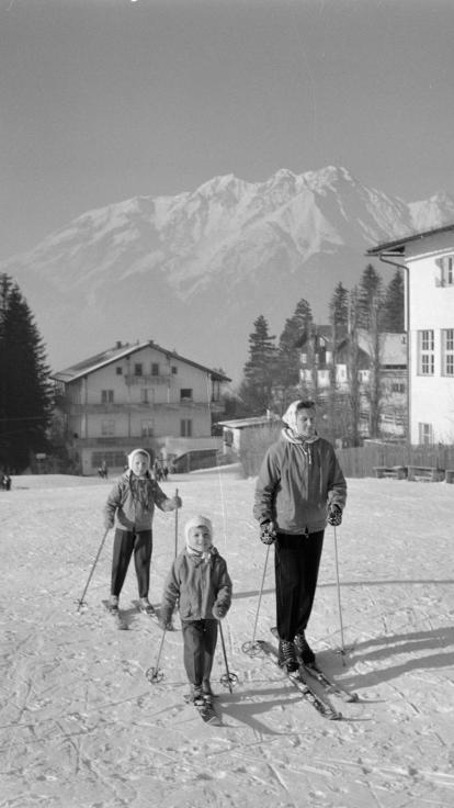 een zwart-witfoto van een moeder met haar twee kinderen op ski's in de sneeuw in Tirol