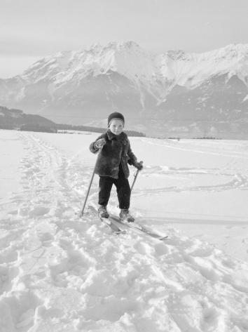 Een zwart-witfoto van een jong kind op ski's in de sneeuw in de bergen