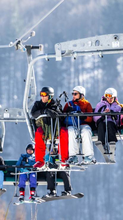 Een foto van vakantiegangers die met hun ski's en snowboards in de lift naar boven zitten