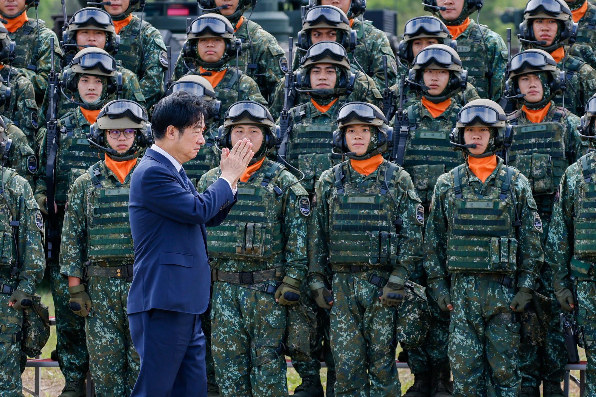 Een foto van de Taiwanese president die met zijn handen plat tegen elkaar gedrukt langs Taiwanese militairen in uniform loopt