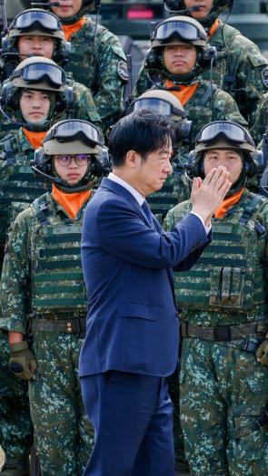 Een foto van de Taiwanese president die met zijn handen plat tegen elkaar gedrukt langs Taiwanese militairen in uniform loopt