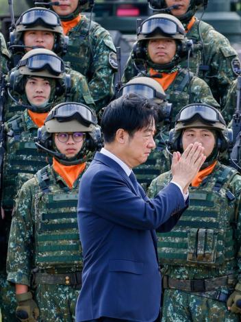 Een foto van de Taiwanese president die met zijn handen plat tegen elkaar gedrukt langs Taiwanese militairen in uniform loopt
