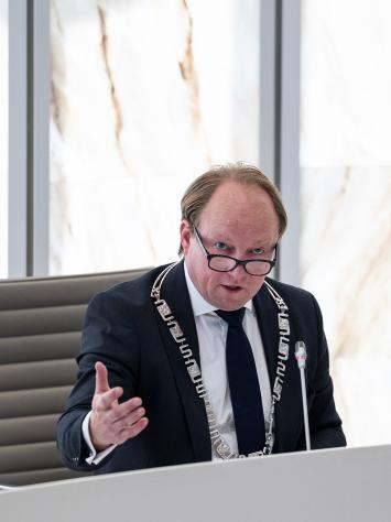 Burgemeester Hein van der Loo tijdens een gemeenteraadsvergadering Almere aan het woord achter microfoon