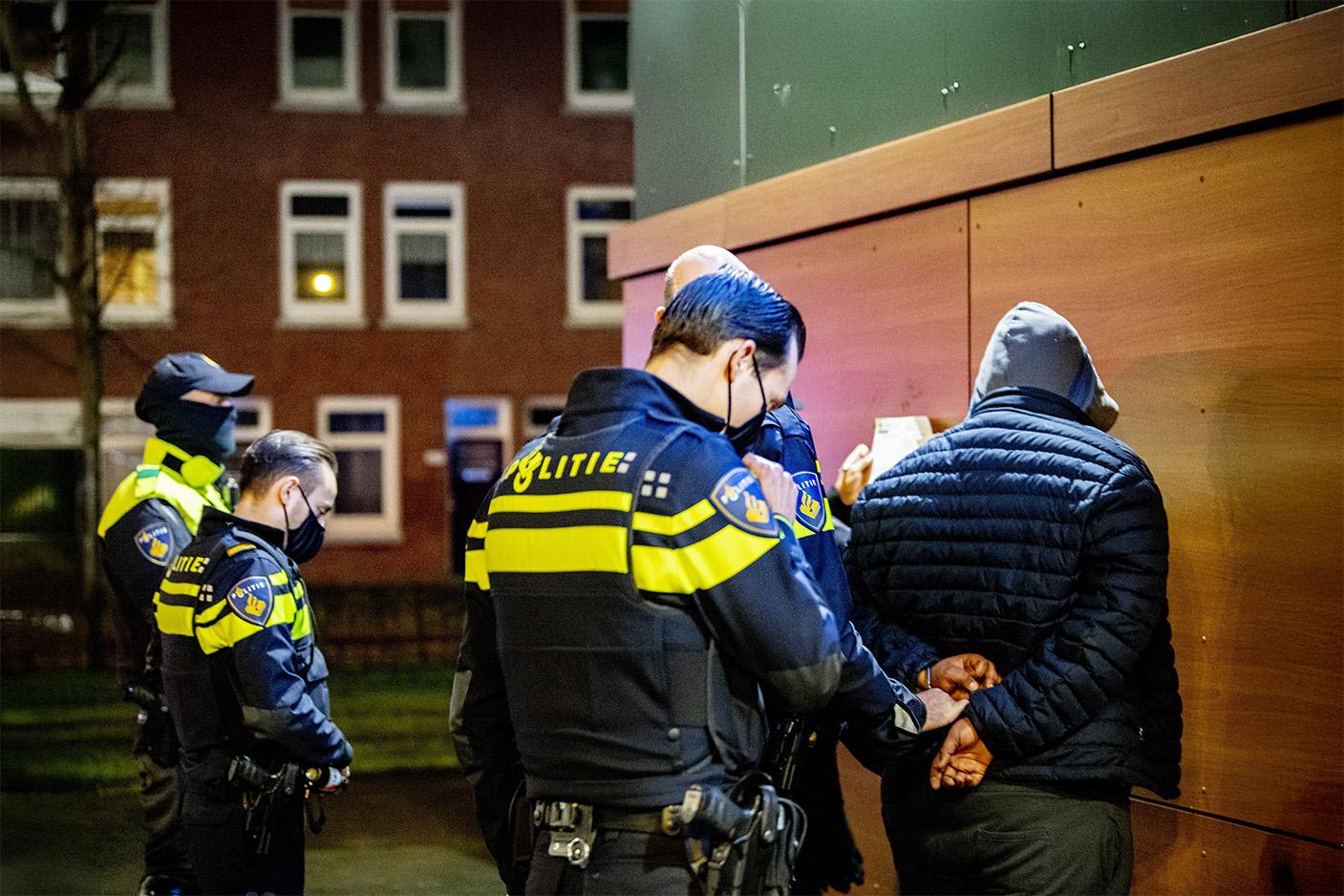 Politie-agenten staan om een man met capuchon heen die met zijn gezicht naar de muur staat en handboeien omkrijgt 