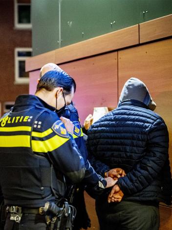 Politie-agenten staan om een man met capuchon heen die met zijn gezicht naar de muur staat en handboeien omkrijgt 