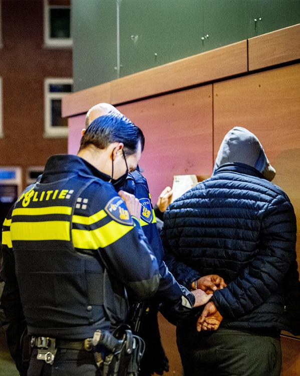 Politie-agenten staan om een man met capuchon heen die met zijn gezicht naar de muur staat en handboeien omkrijgt 