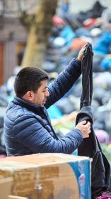 Man zoekt kleding uit tussen een vuilnisbelt vol met dozen en zakken met andere kleding