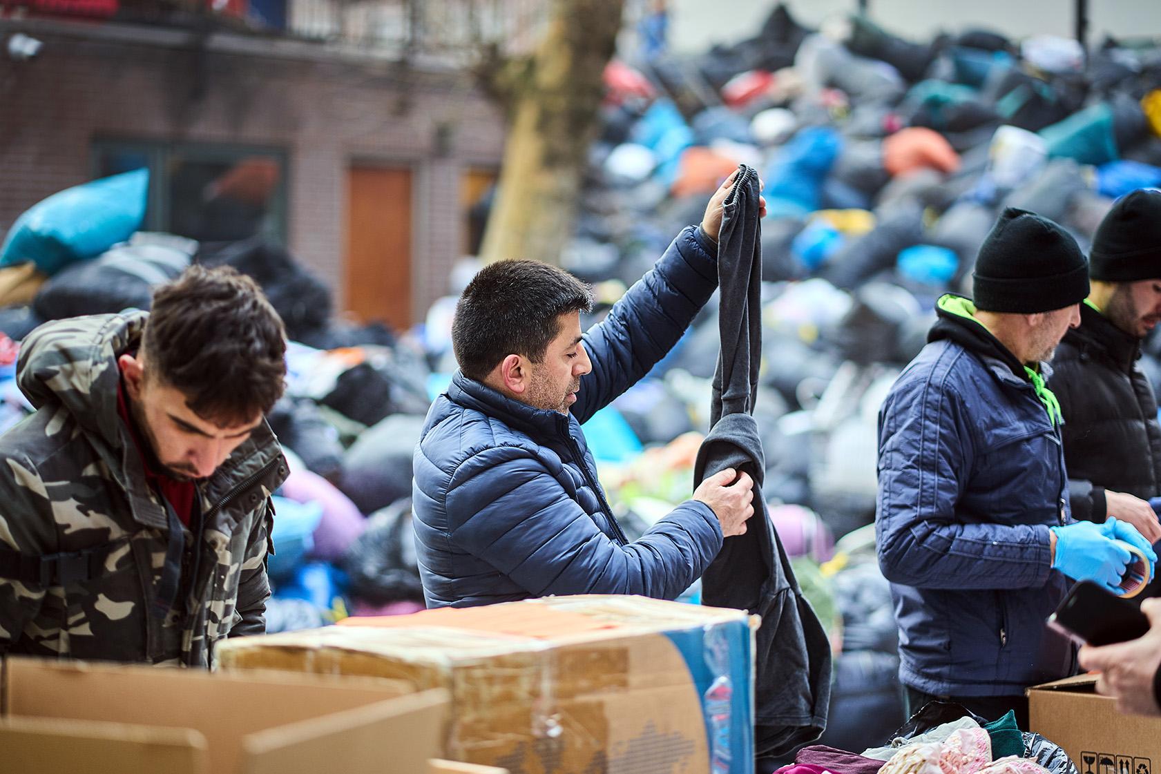 Man zoekt kleding uit tussen een vuilnisbelt vol met dozen en zakken met andere kleding