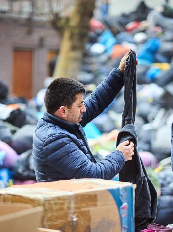 Man zoekt kleding uit tussen een vuilnisbelt vol met dozen en zakken met andere kleding