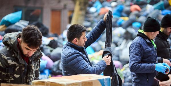 Man zoekt kleding uit tussen een vuilnisbelt vol met dozen en zakken met andere kleding
