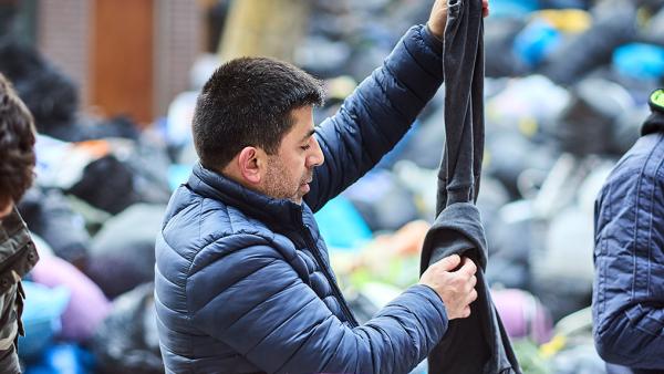 Man zoekt kleding uit tussen een vuilnisbelt vol met dozen en zakken met andere kleding