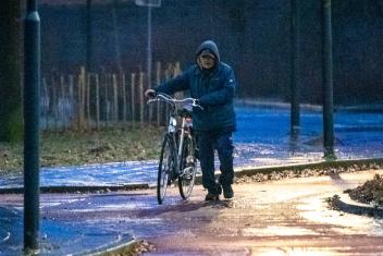 Een man loopt met zijn fiets aan de hand over een glad fietspad heen 